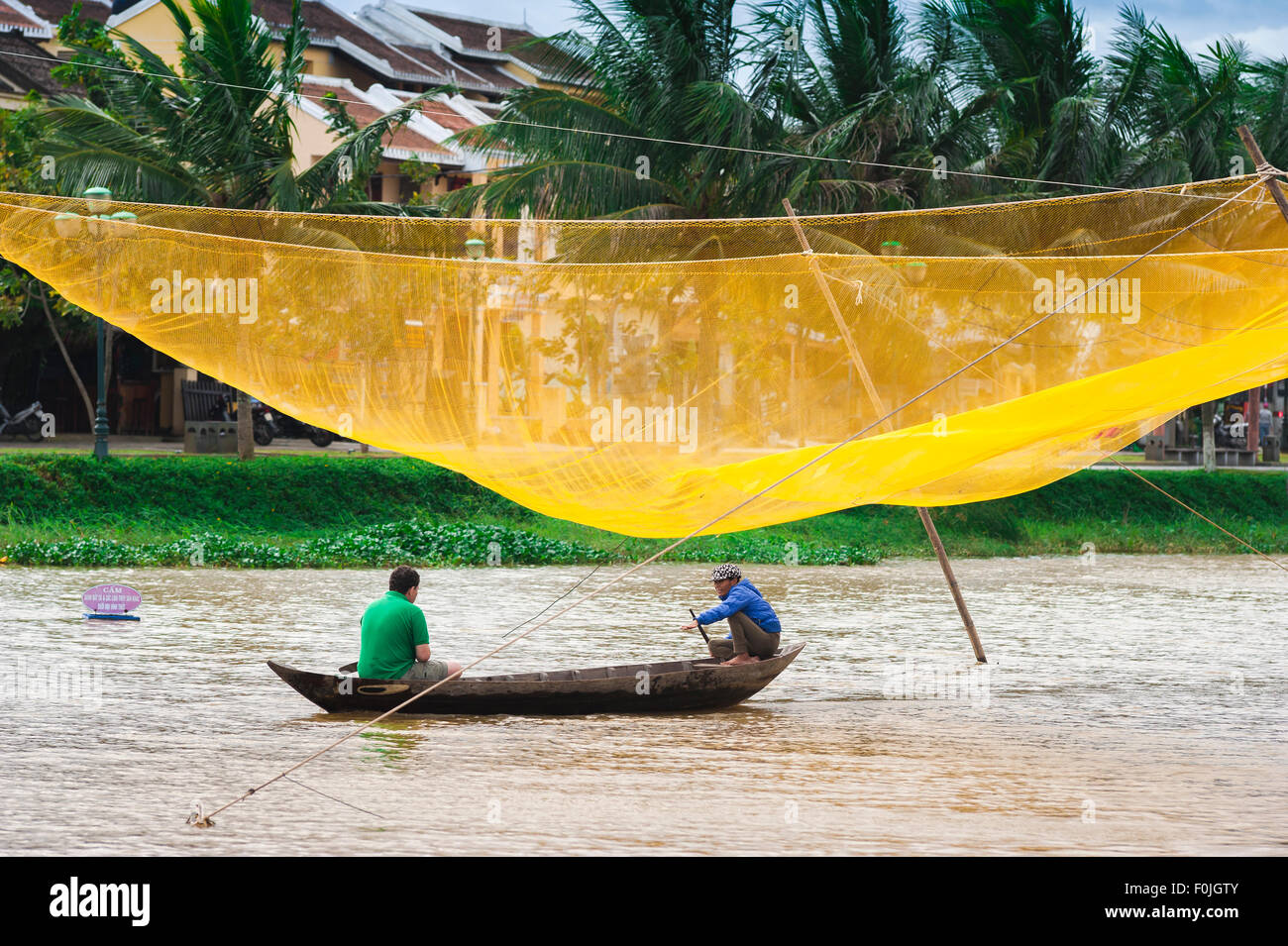 Hoi An river boat, a tourist takes a boat ride along the Thu Bon River in Hoi An passing by a huge yellow fishing net, Central Coast, Vietnam Stock Photo