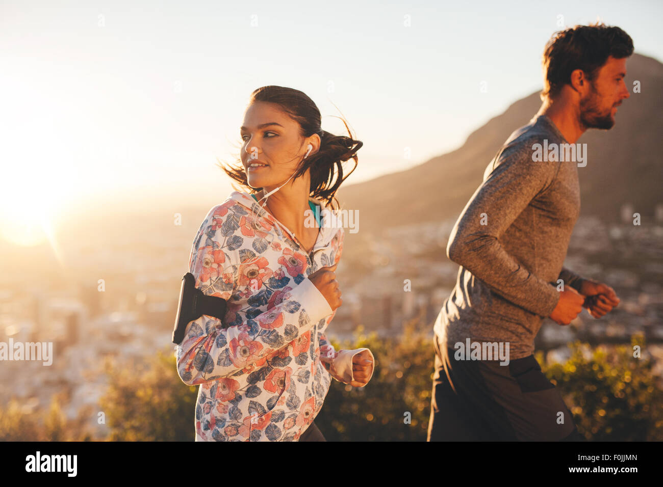 Young woman looking back while running with a man outdoors. Couple on morning run. Stock Photo