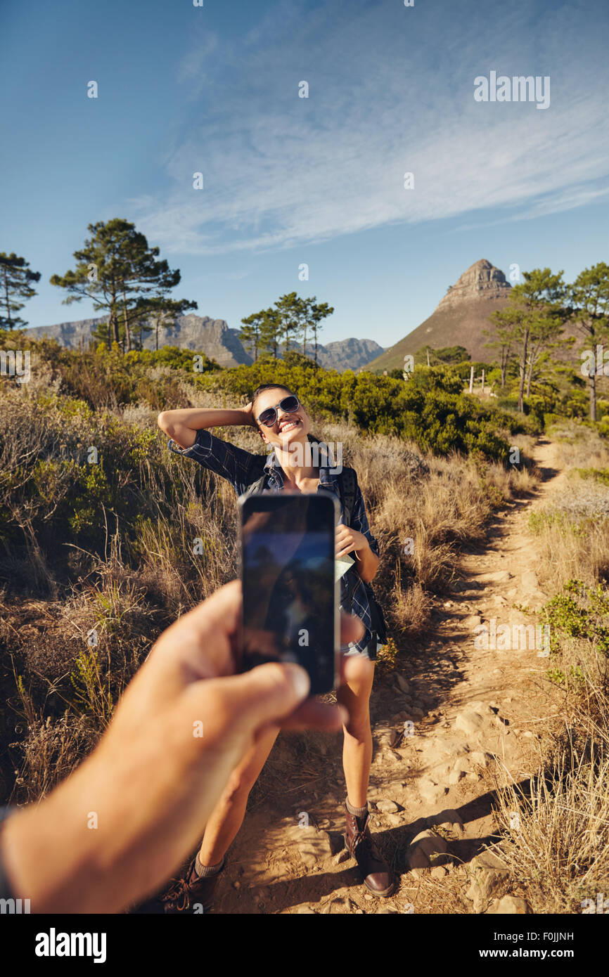 Young woman posing to mobile phone camera. Man hand holding a smart phone taking pictures on a young woman. Couple hiking in cou Stock Photo