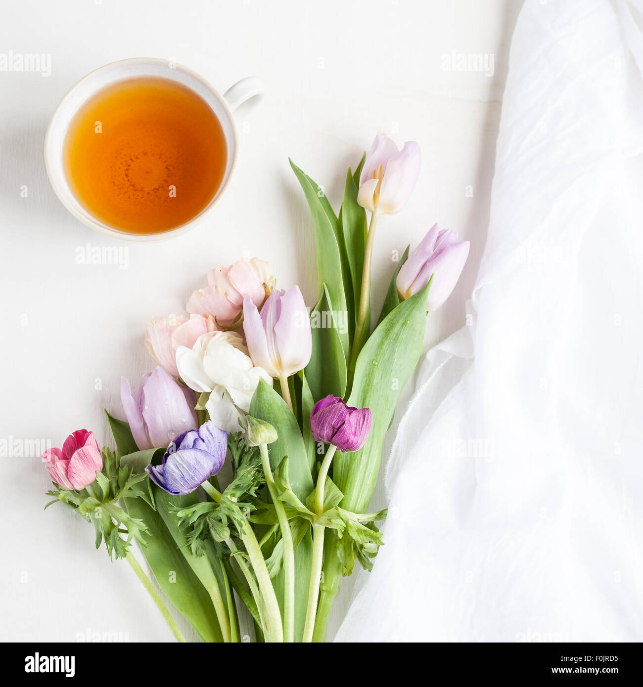 a bunch of spring flowers, anemones and tulips, with a cup of tea and some fabric Stock Photo
