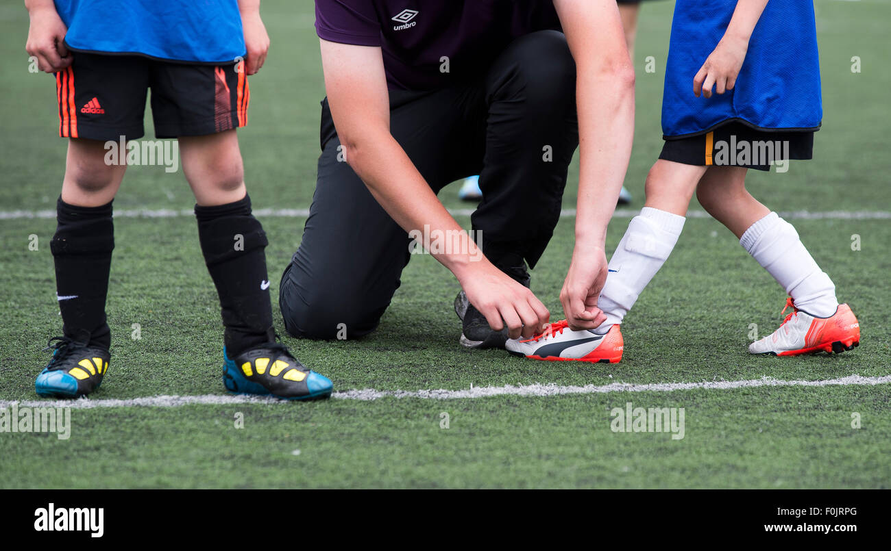 A sports teacher ties the boot laces of a young child during a game of football. Stock Photo