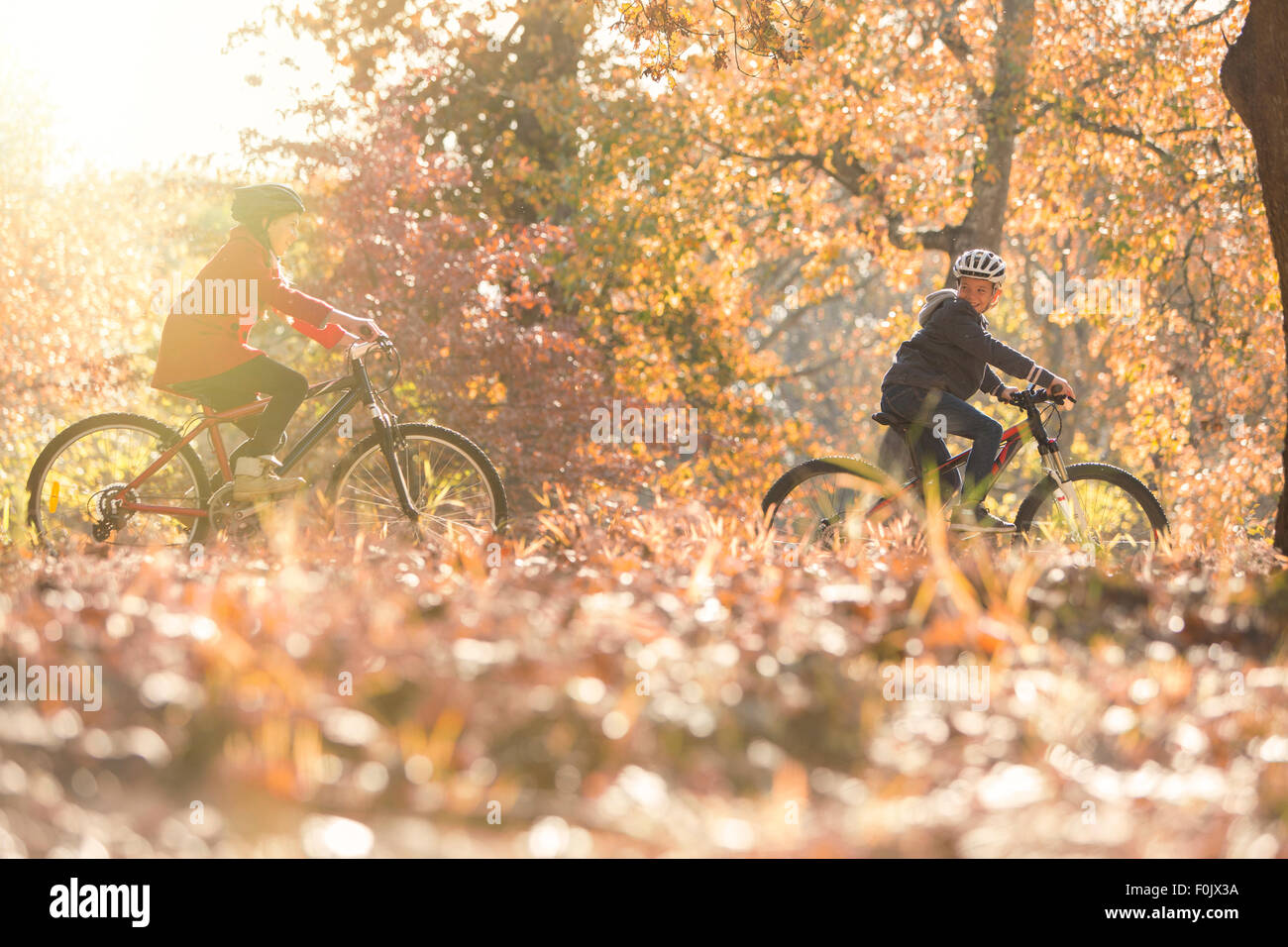 Boy and girl riding bikes in autumn leaves Stock Photo