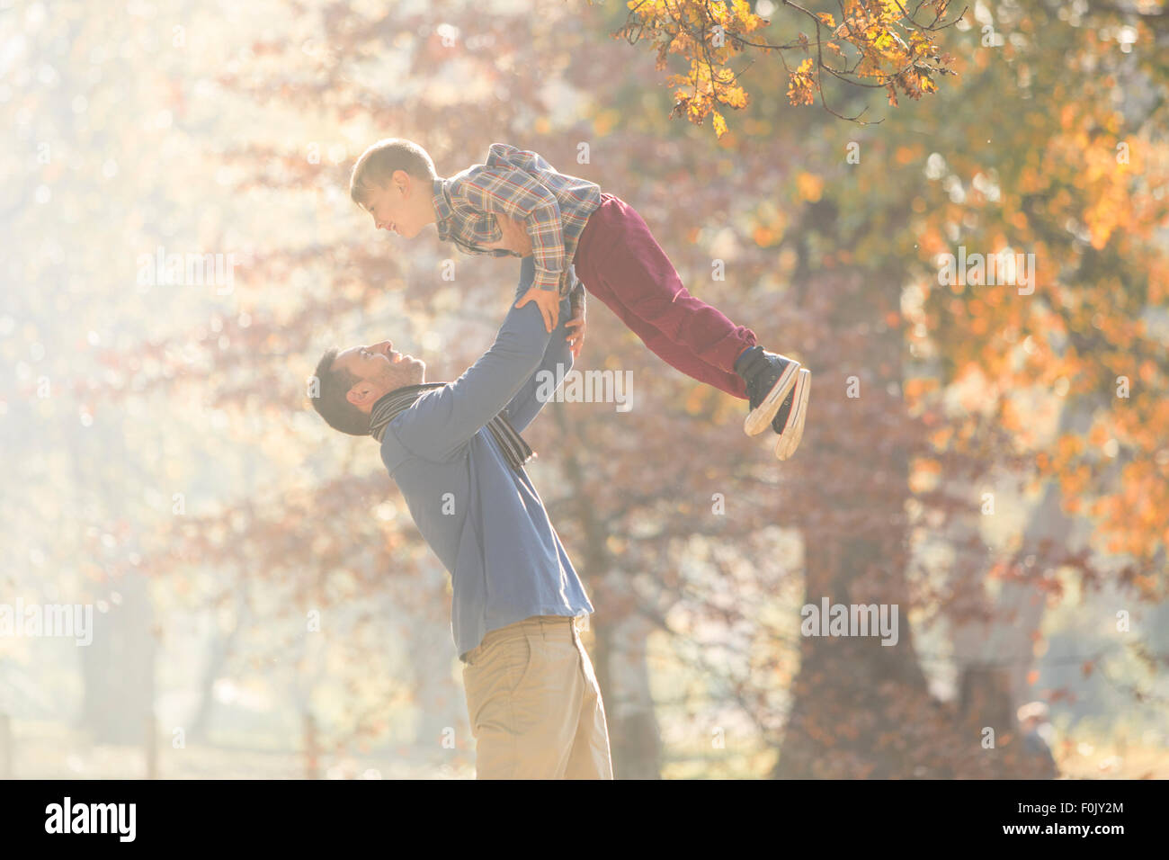 Father lifting son overhead in woods with autumn leaves Stock Photo