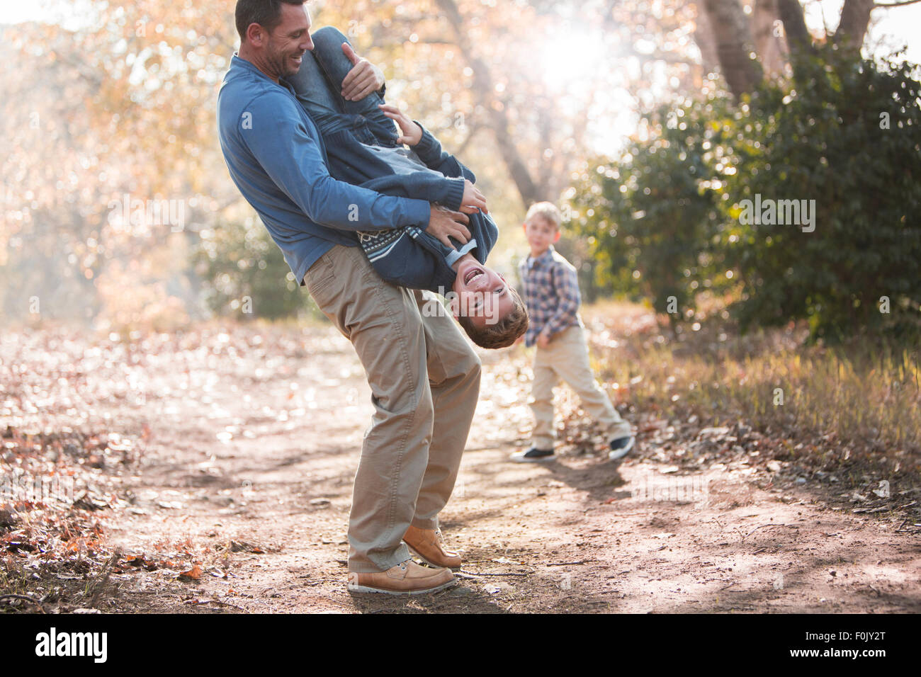 Playful father lifting son upside-down on path in woods Stock Photo