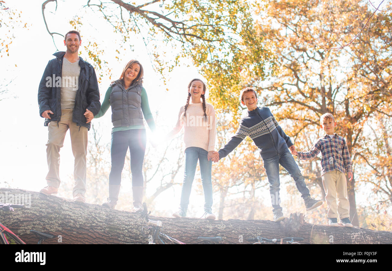 Portrait smiling family holding hands on fallen log in a row Stock Photo