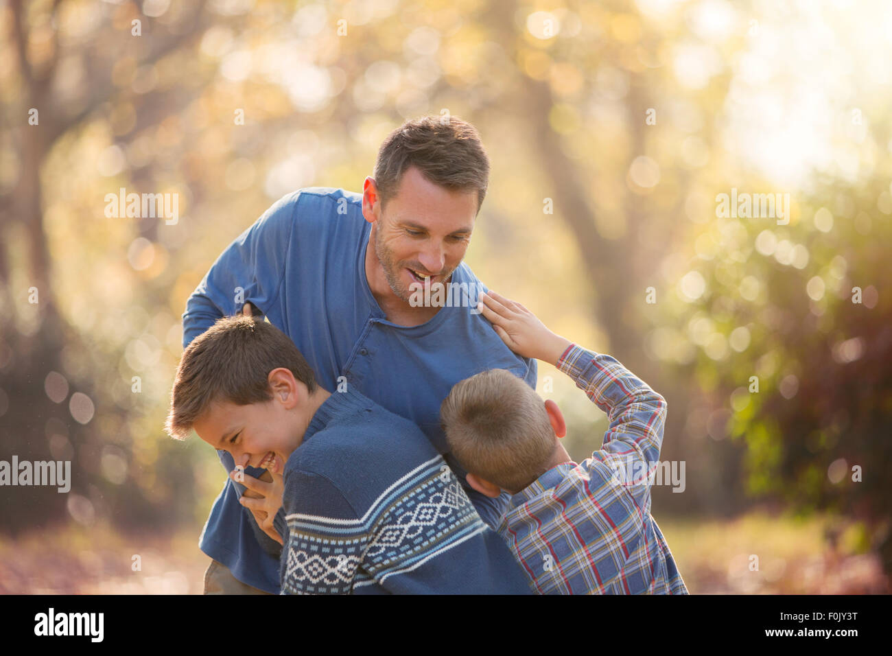 Playful father and sons rough housing outdoors Stock Photo