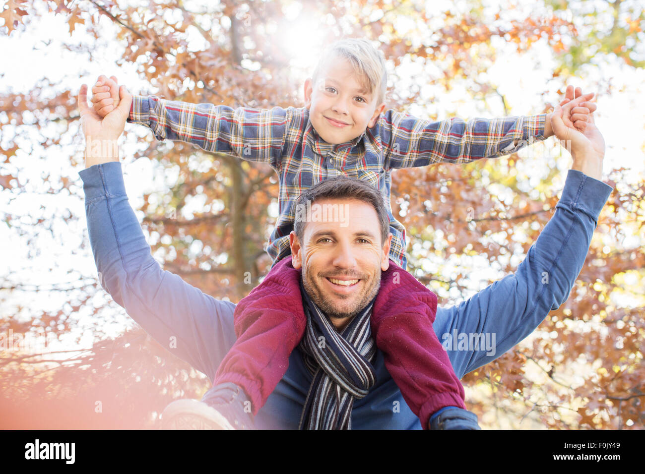 Portrait smiling father carrying son on shoulders below autumn leaves Stock Photo