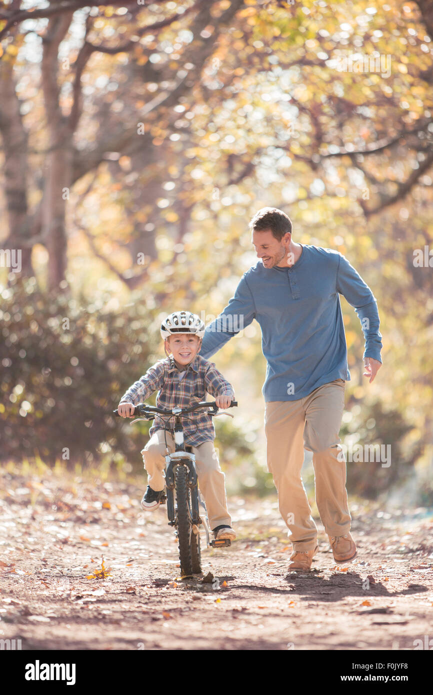 Father teaching son to ride a bicycle on path in woods Stock Photo
