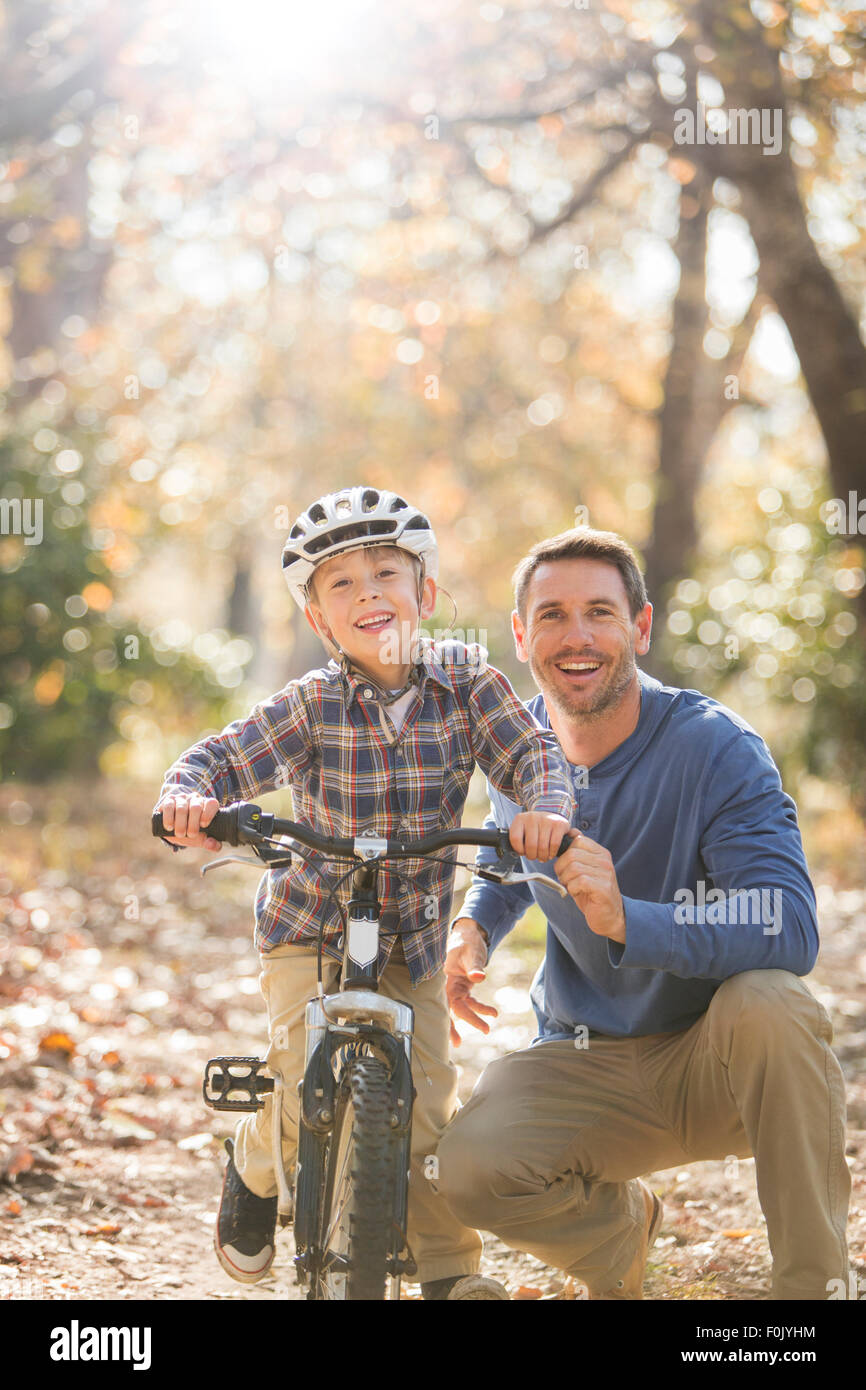 Portrait smiling father teaching son to ride a bike in woods Stock Photo