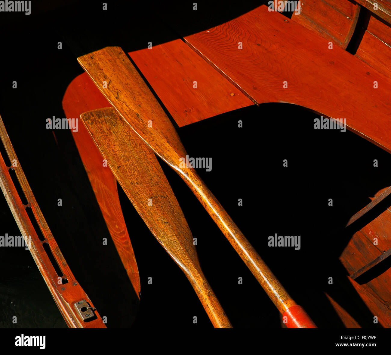 Vintage wooden boat in sun, harsh shadows, oars, seats. Stock Photo