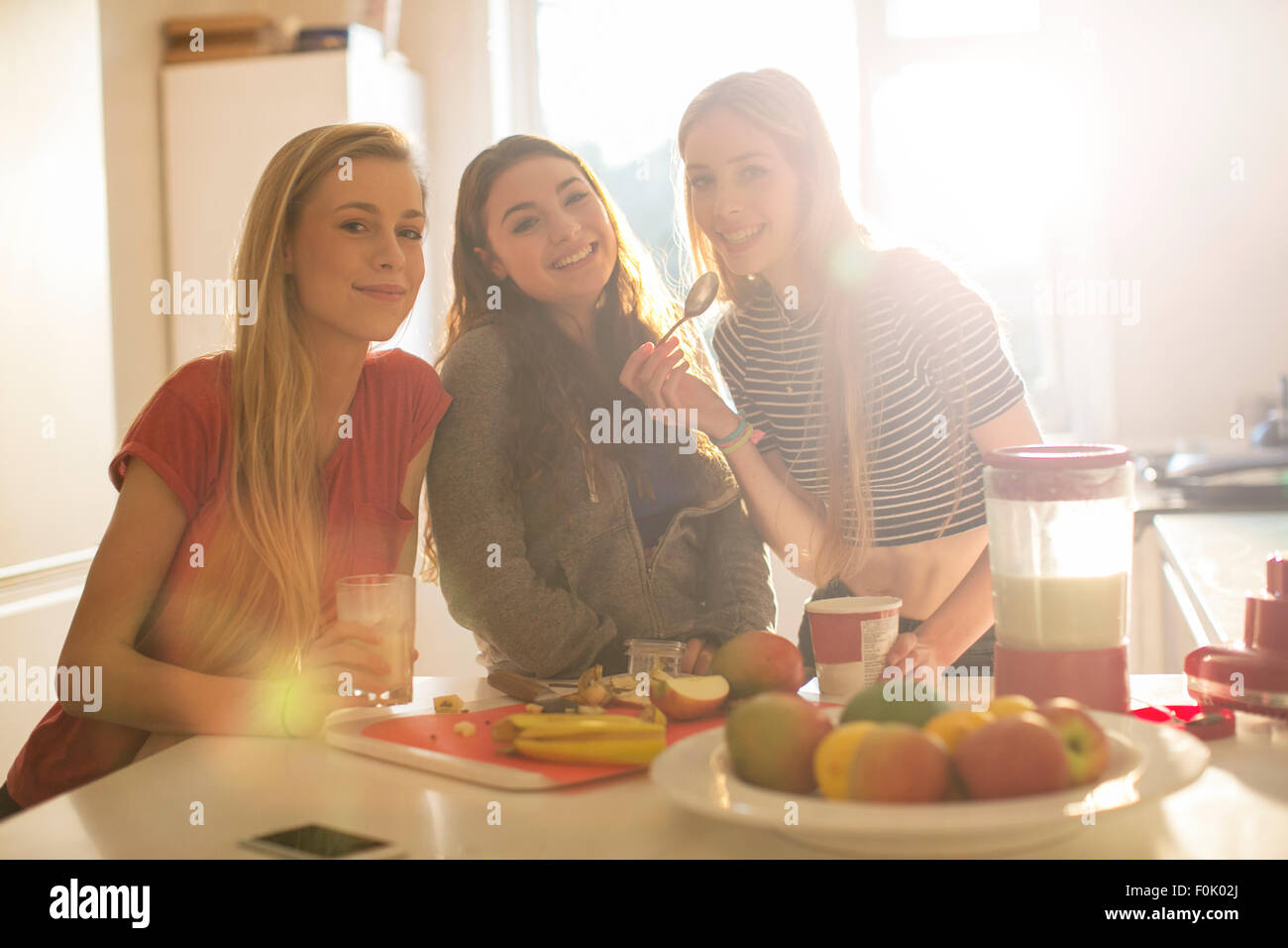 Portrait teenage girls eating in sunny kitchen Stock Photo