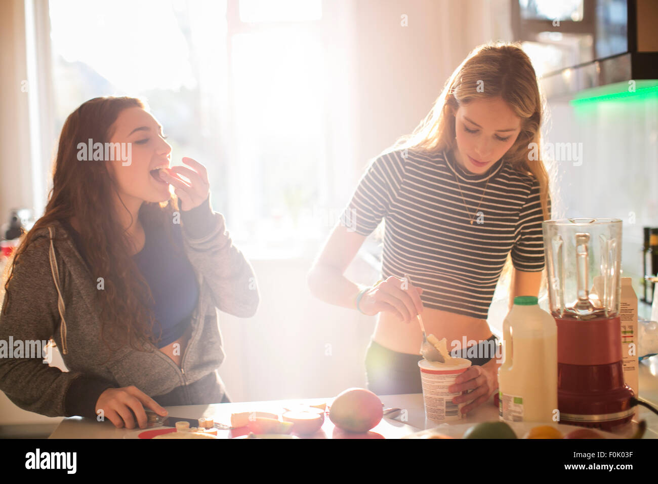 Teenage girls making smoothie in sunny kitchen Stock Photo