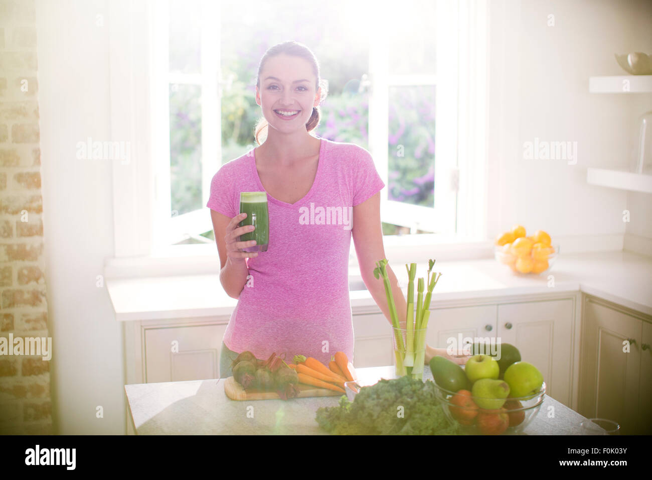 Portrait smiling woman drinking green smoothie in kitchen Stock Photo