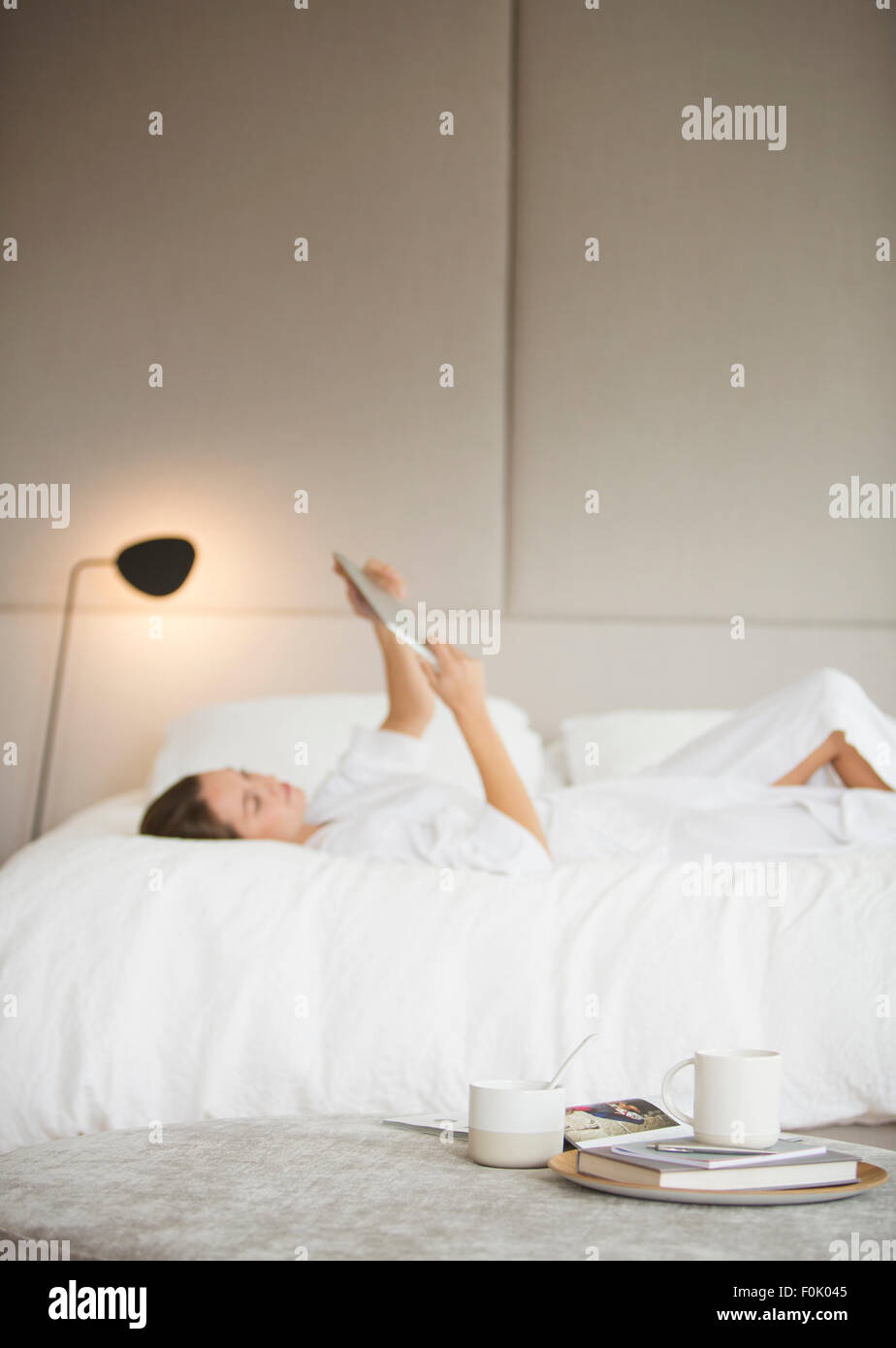Woman in bathrobe laying on bed using digital tablet Stock Photo