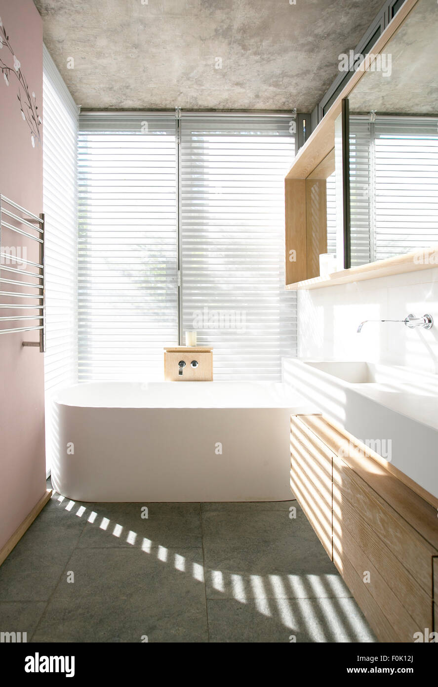 Light through blinds behind soaking tub in modern bathroom Stock Photo