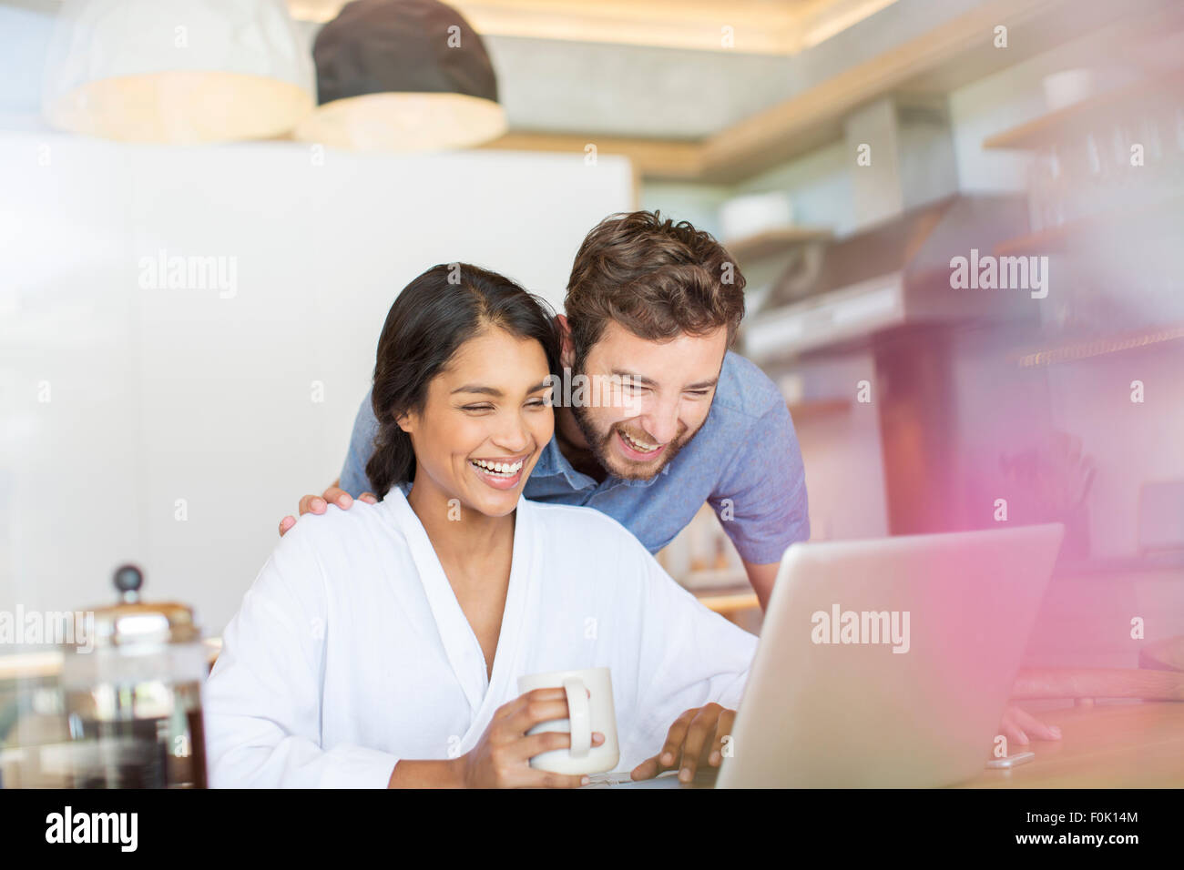 Laughing couple drinking coffee and using laptop Stock Photo