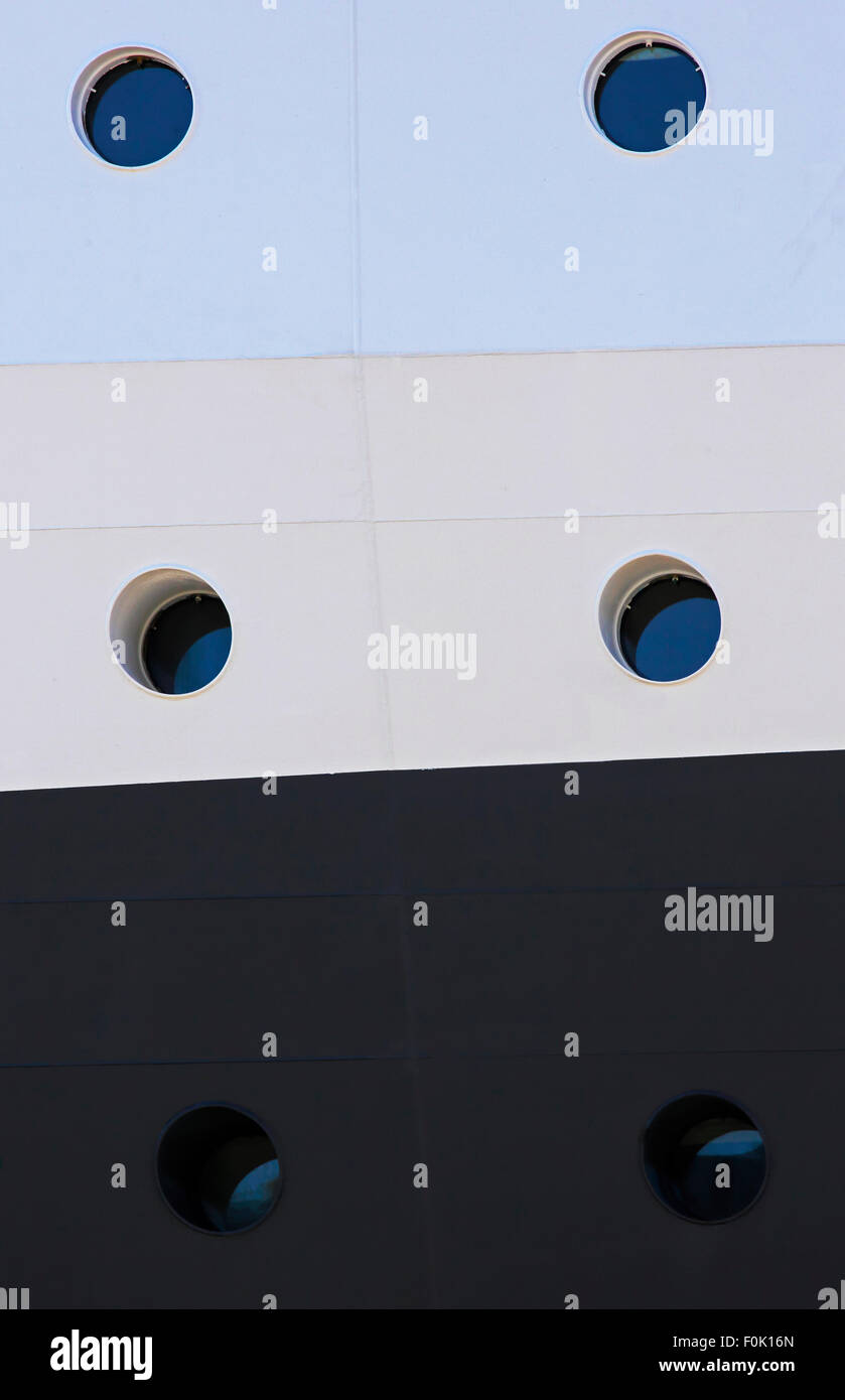 Six portholes on a multi-colored side of a cruise ship. Stock Photo
