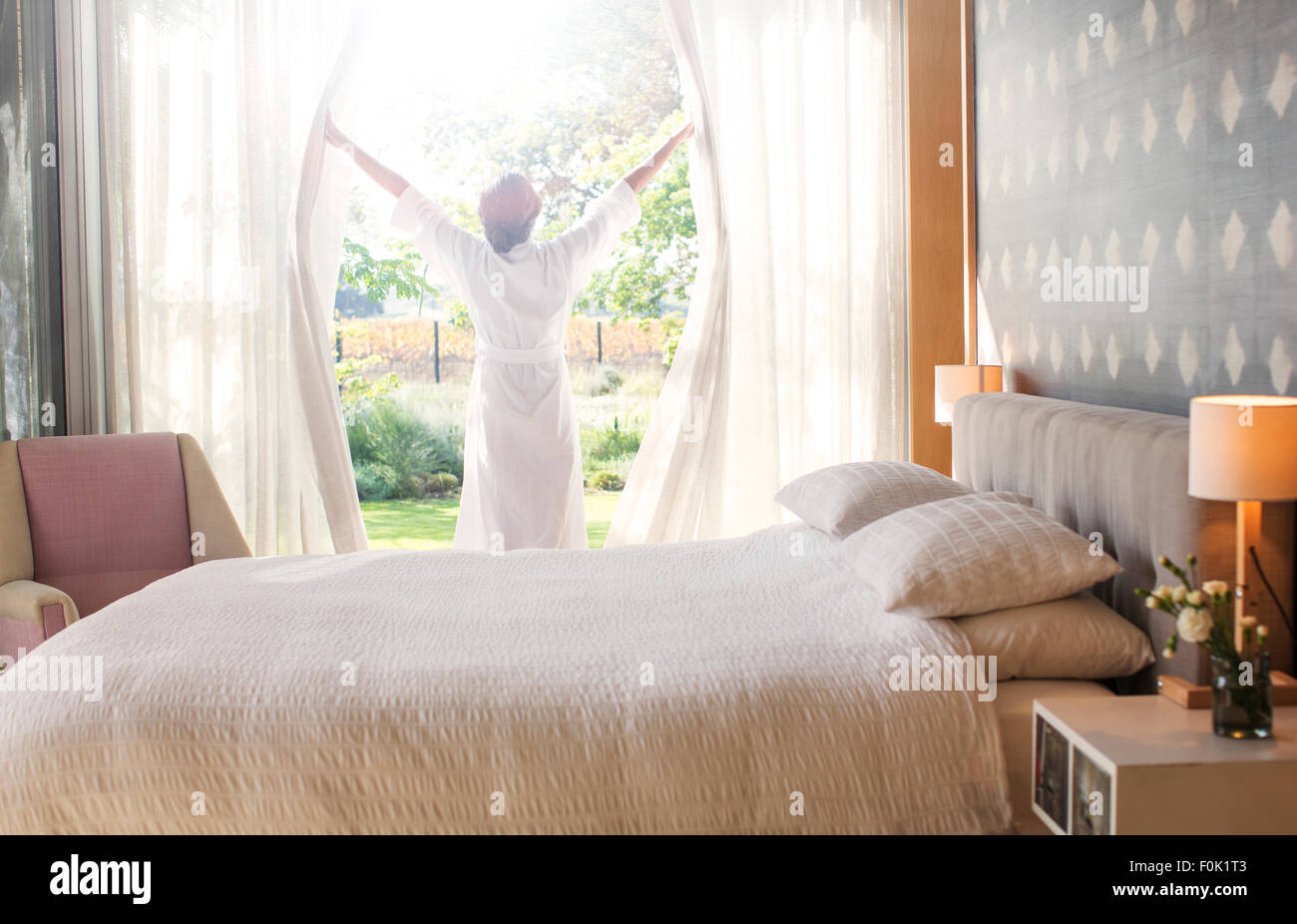 Woman in bathrobe opening bedroom curtains Stock Photo