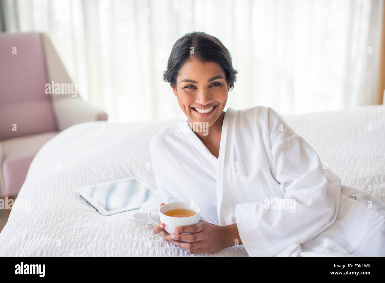 Portrait smiling woman in bathrobe drinking tea on bed Stock Photo