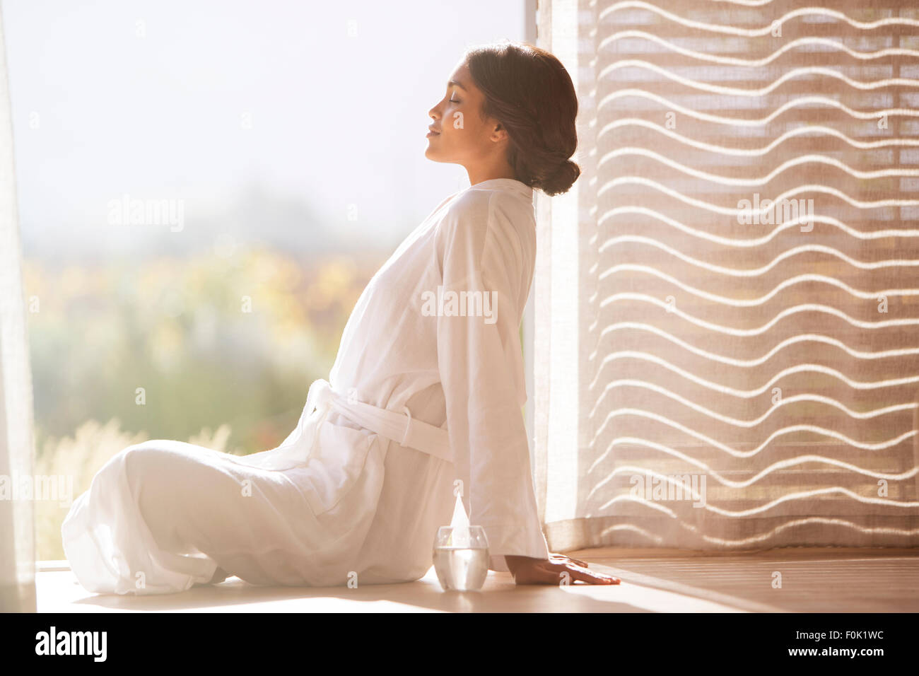 Serene woman in bathrobe sitting cross-legged at sunny doorway Stock Photo