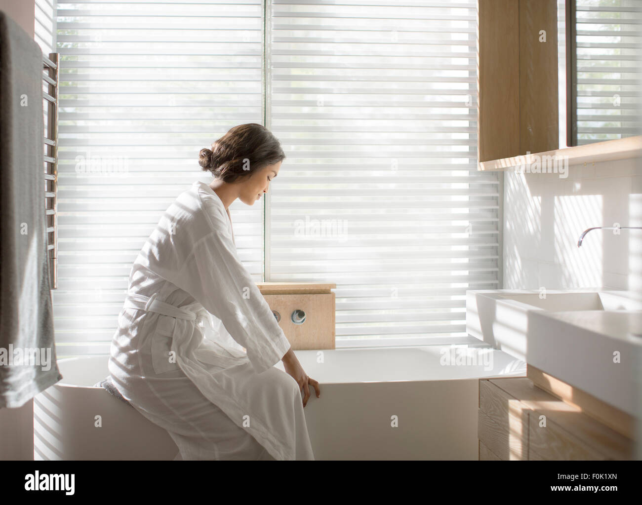 Woman in bathrobe drawing a bath in soaking tub in luxury bathroom Stock Photo