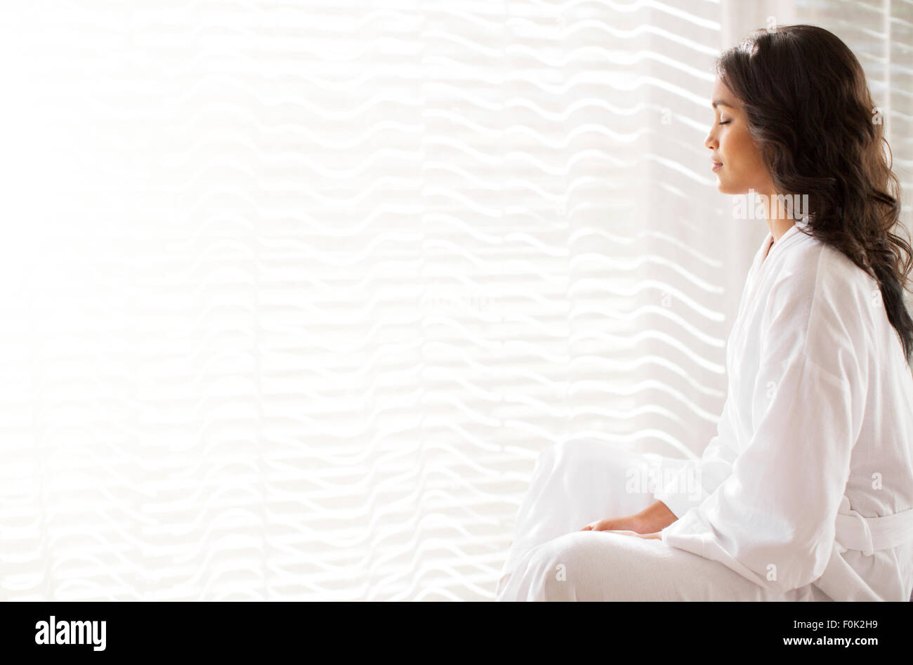 Serene woman in bathrobe meditating at sunny window Stock Photo