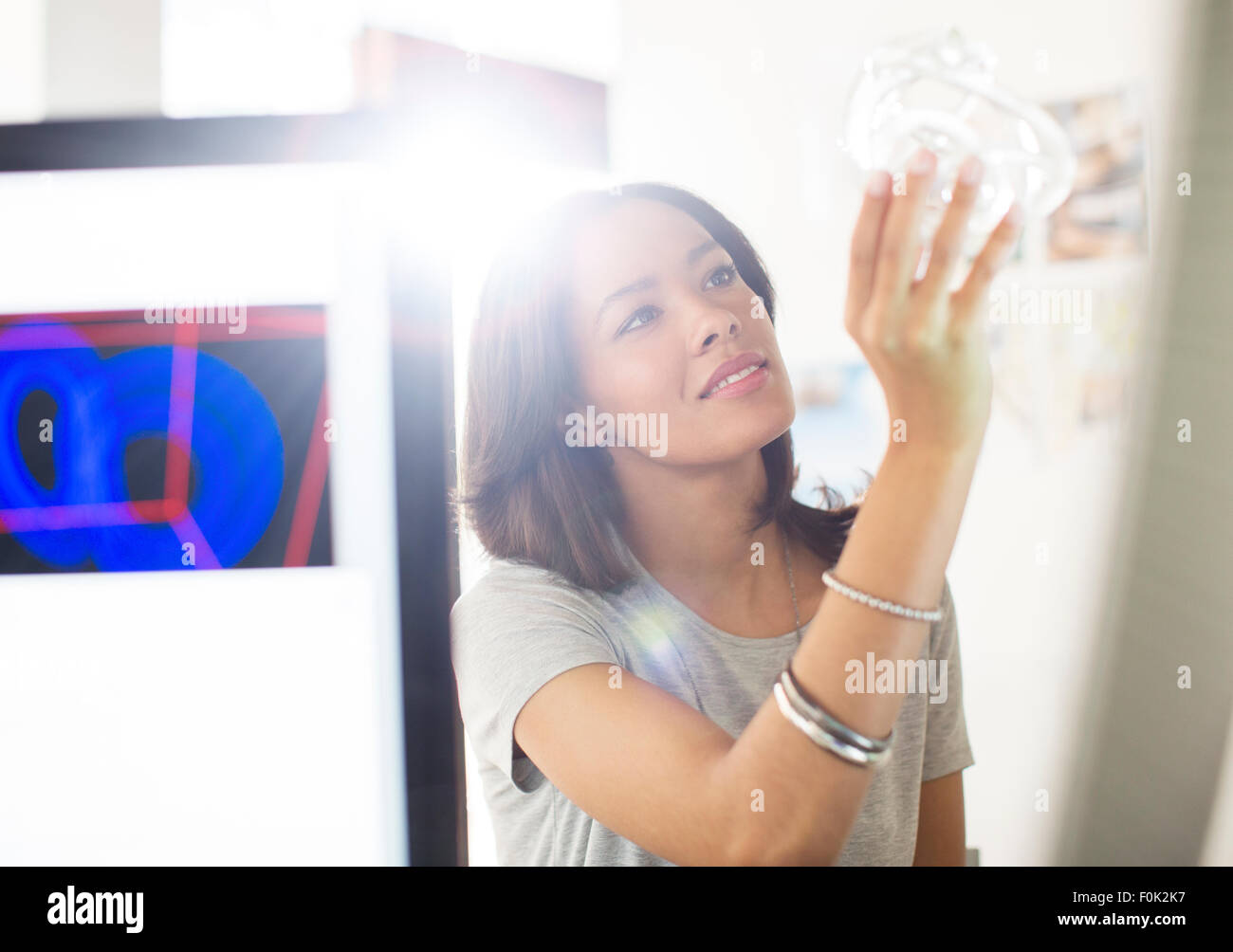 Curious businesswoman examining glass in sunny office Stock Photo