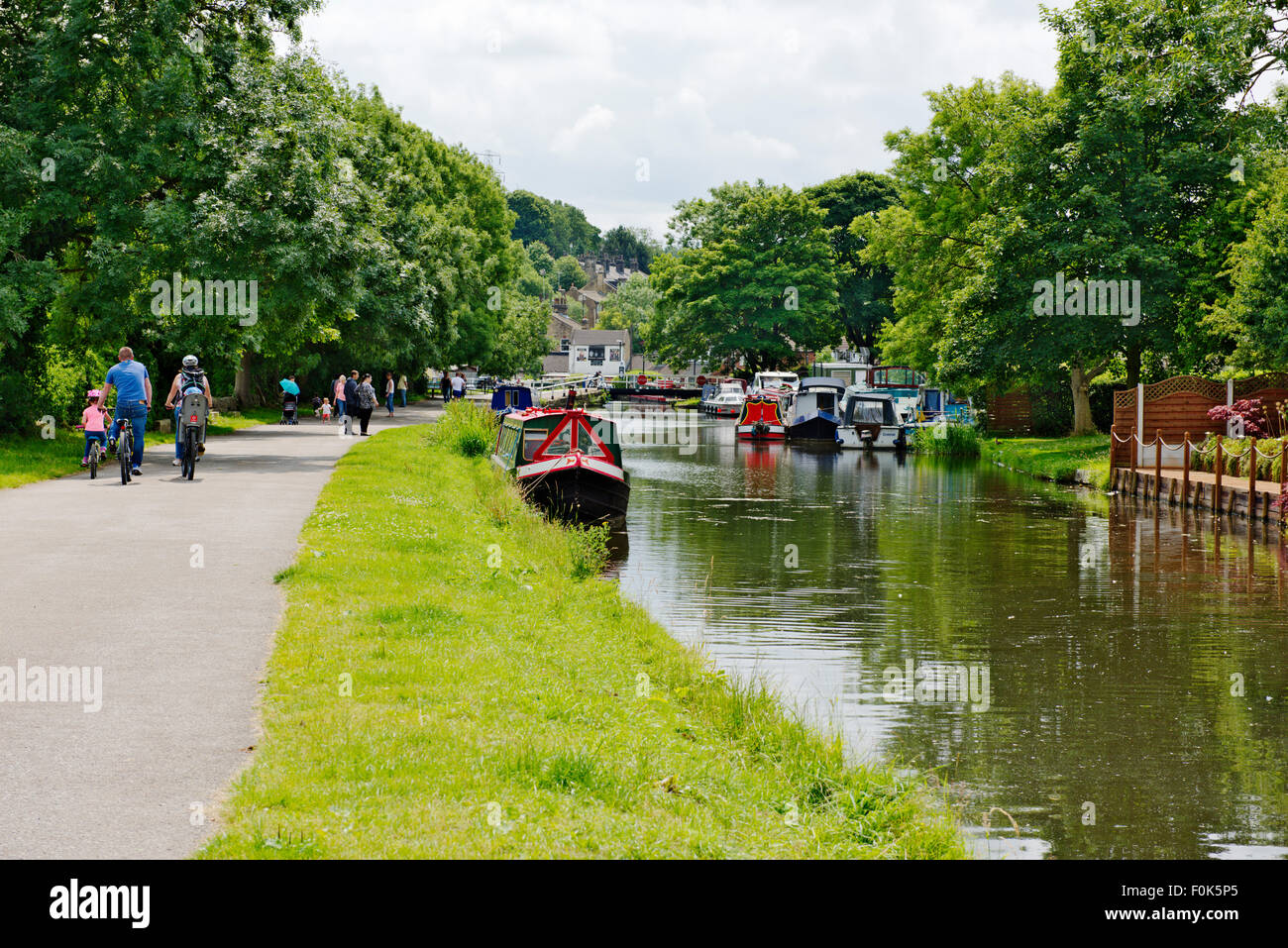 Families walking, cycling along Leeds and Liverpool canal tow-path on sunny summer day, near Calverley Bridge, West Yorkshire Stock Photo