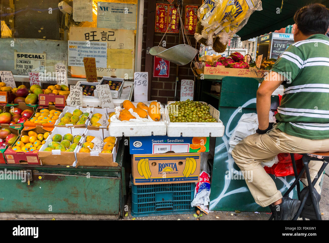 New York City, USA, Clerk outside Chinese neighborhood grocery Food store  in Chinatown District, Man, Sitting, from Behind, migrants nyc, neighborhood stores, display, fresh food Stock Photo