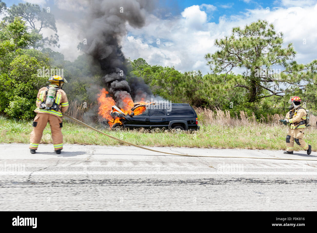 Firefighter putting out the car fire on the side of the highway Stock Photo