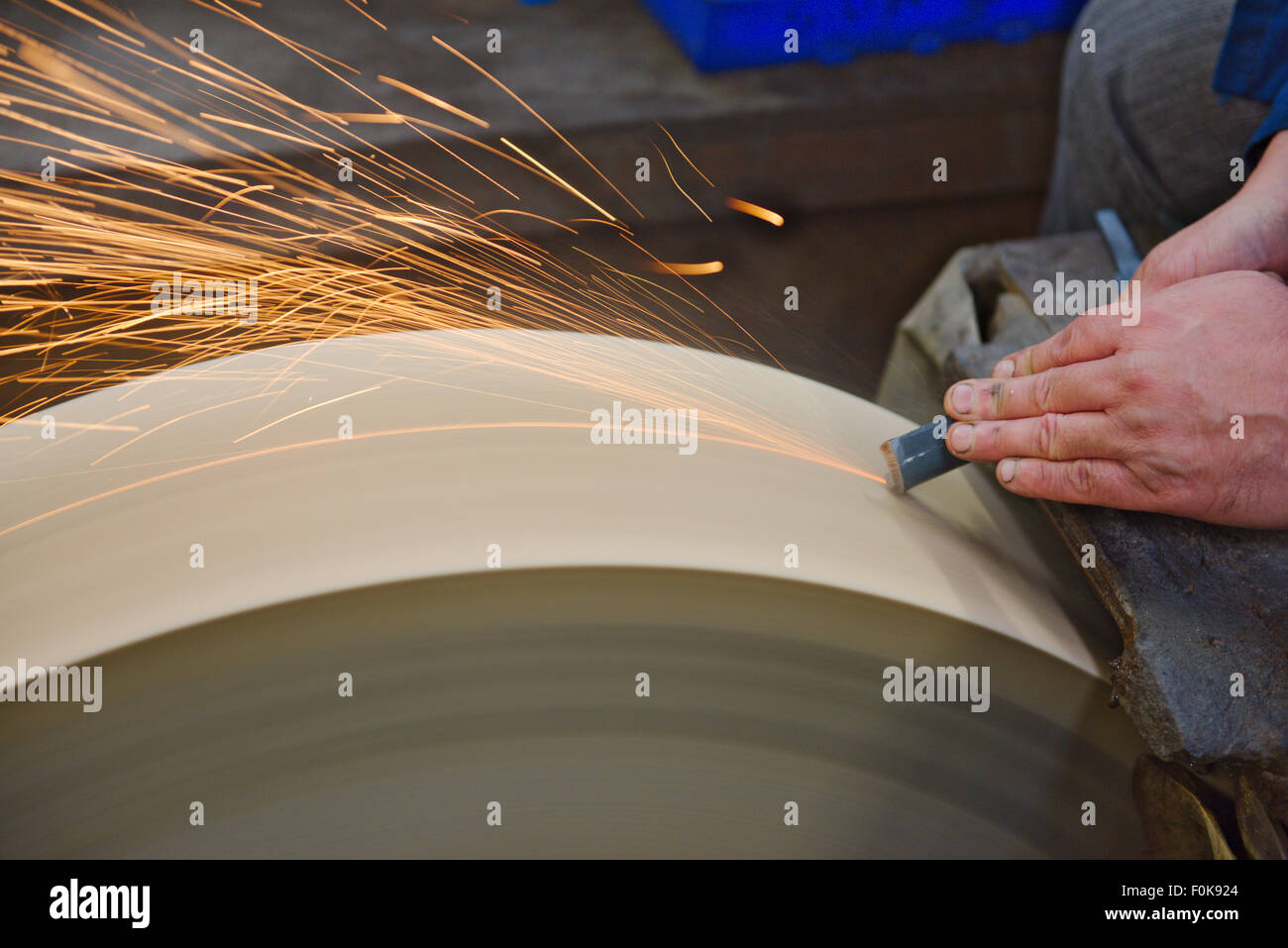 Man rough grinding tool during manufacturing using a large wetstone grinder, Sheffield, UK Stock Photo