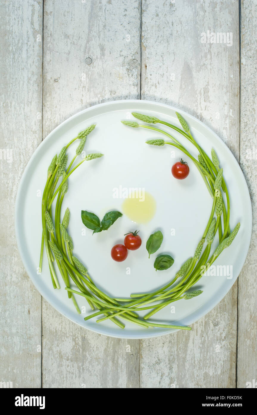 Wild asparagus on plate, olive oil, tomatoes and basil Stock Photo