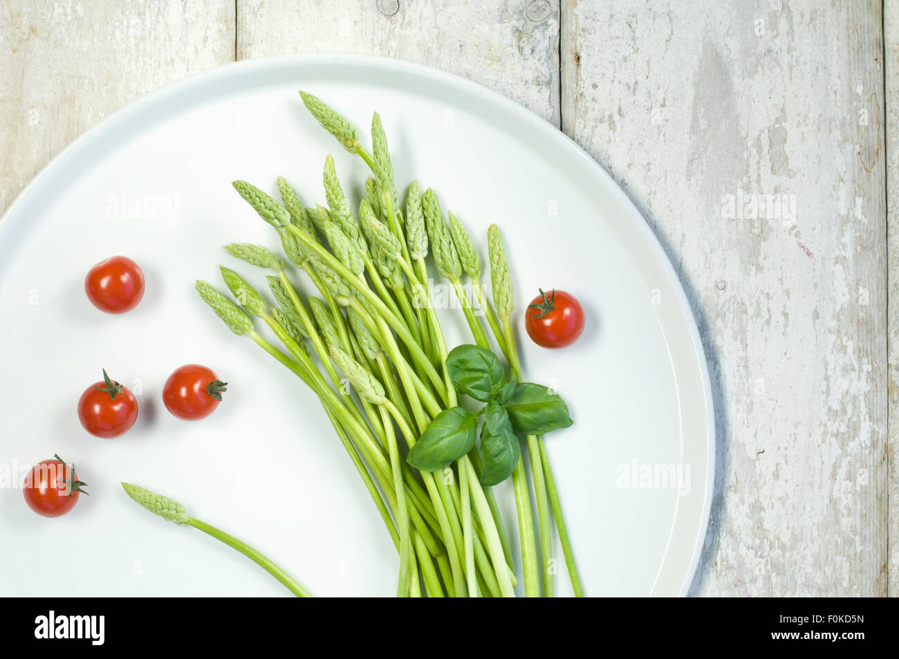 Wild asparagus on plate, tomatoes and basil Stock Photo