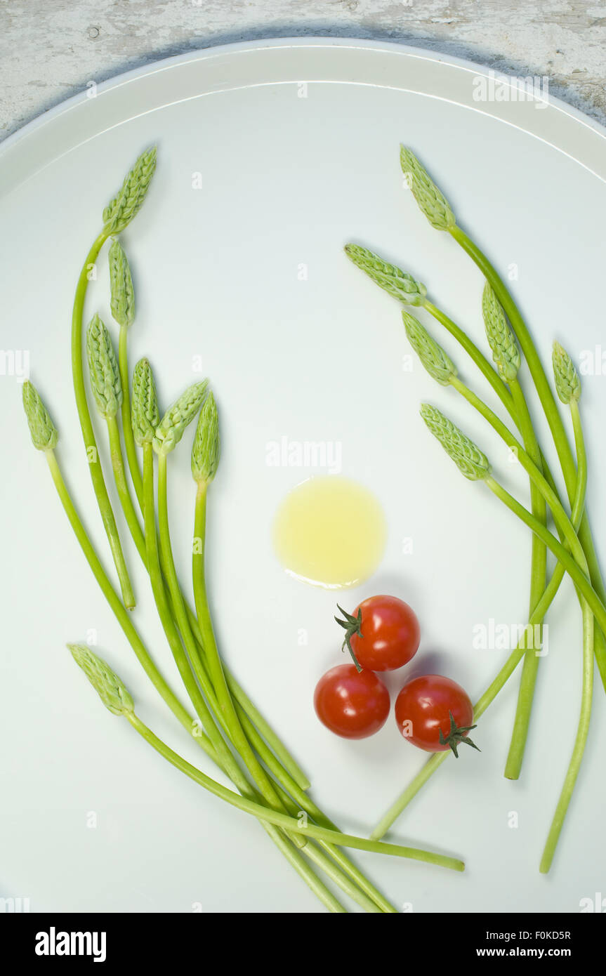 Wild asparagus on plate, olive oil and tomatoes Stock Photo