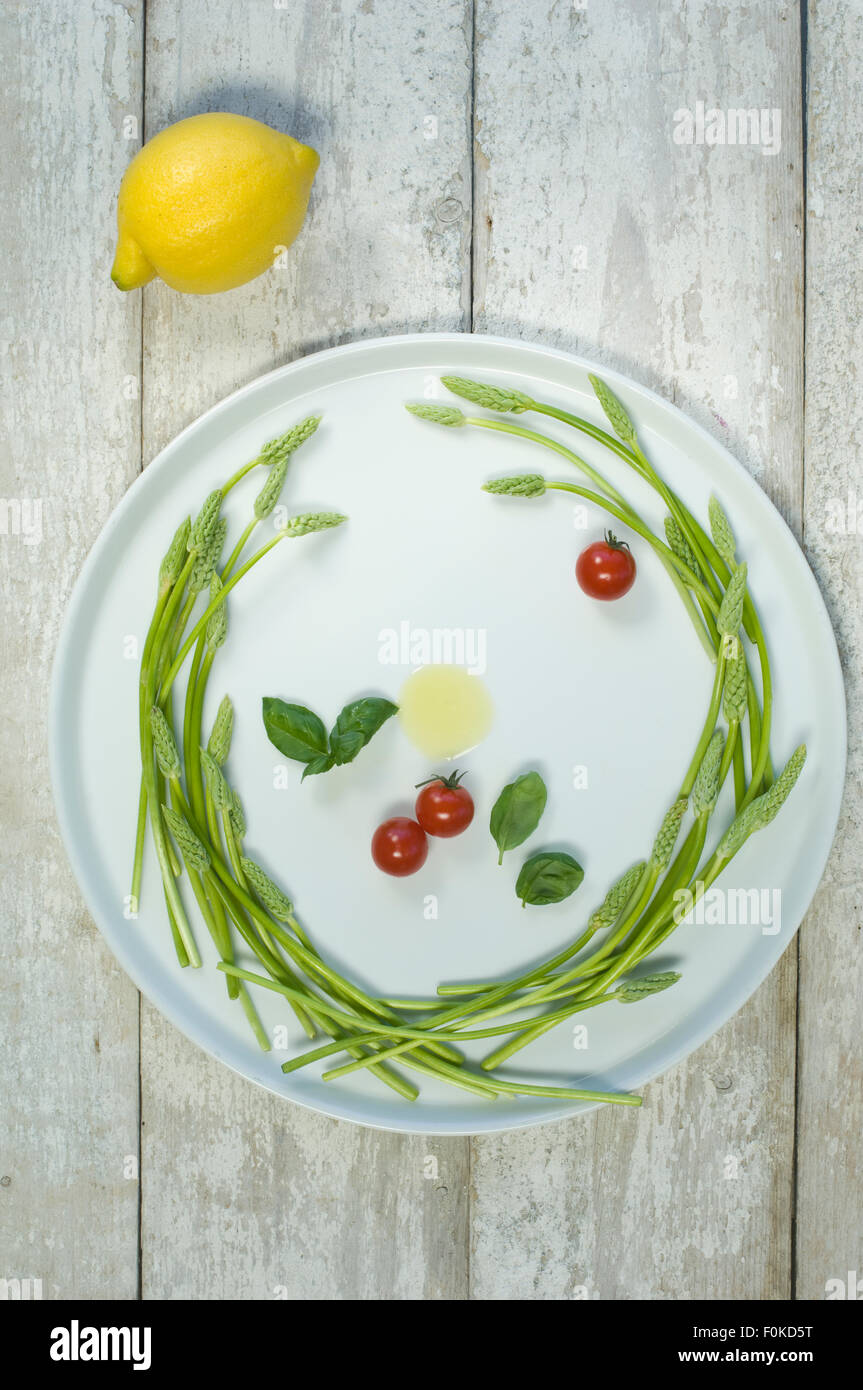 Wild asparagus, olive oil, tomatoes and basil on plate, lemon on wood Stock Photo
