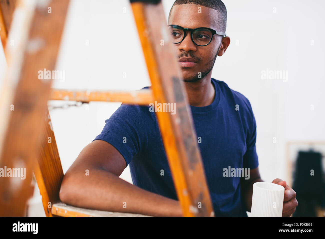 Young man leaning on step ladder having a coffee break Stock Photo