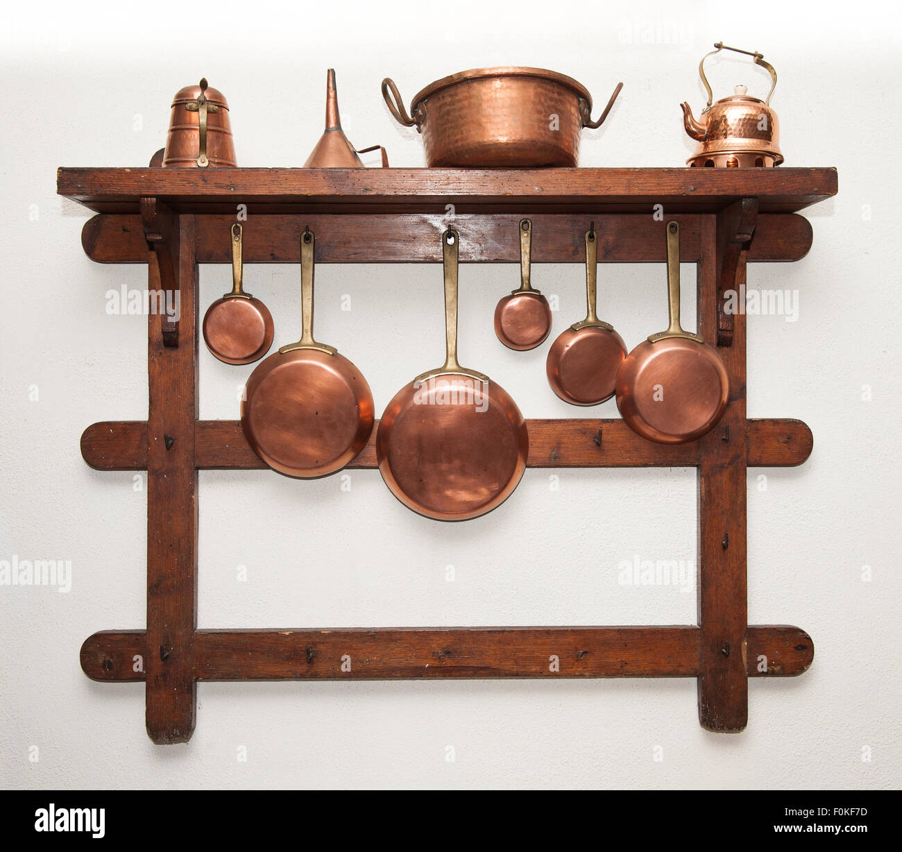 Different kind of vintage copper cookware, pans, coffee pot and funnel hung on wooden shelf in kitchen Stock Photo