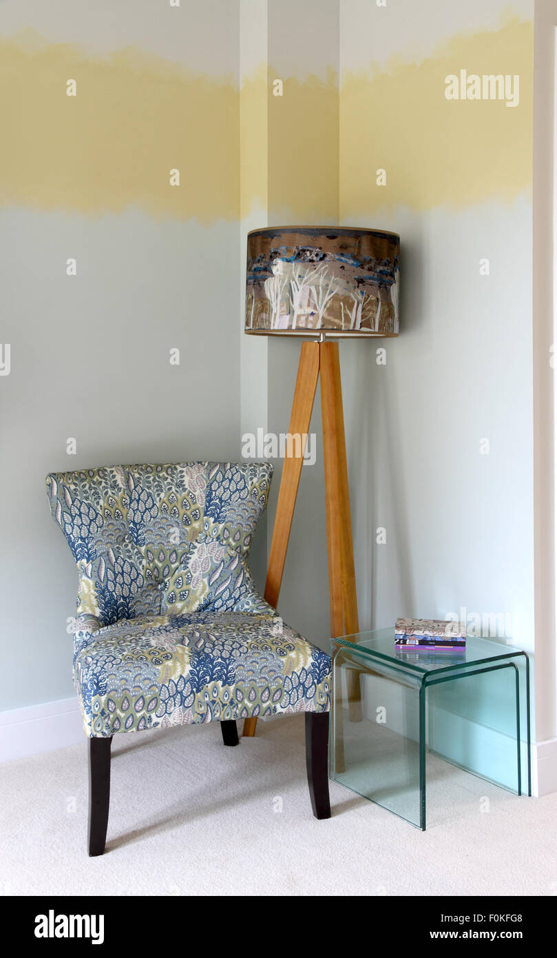 Room corner with three legged standard lamp with abstract shade,easy chair and next of glass tables Stock Photo