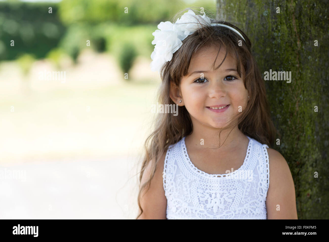 Portrait of smiling little girl leaning on a tree Stock Photo - Alamy
