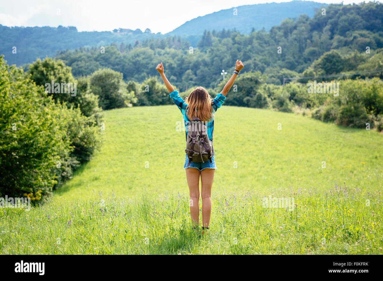 Alto Adige, back view of teenage girl with arms up standing on a meadow ...