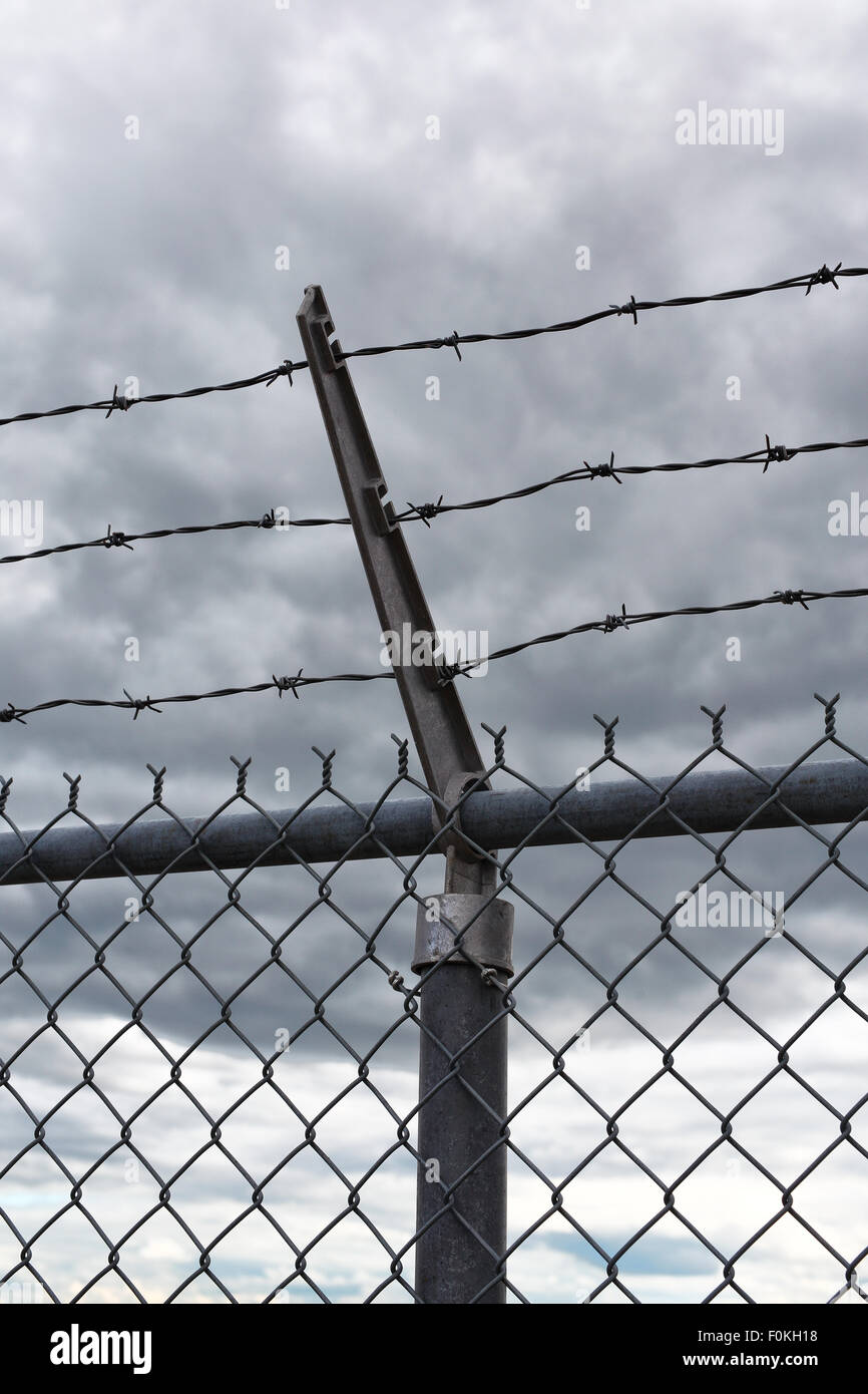 A view of the sky with dark clouds behind a barbed wire security fence ...