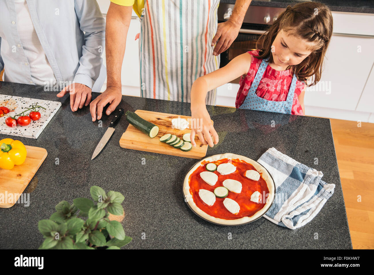 Little girl garnishing homemade pizza in the kitchen Stock Photo