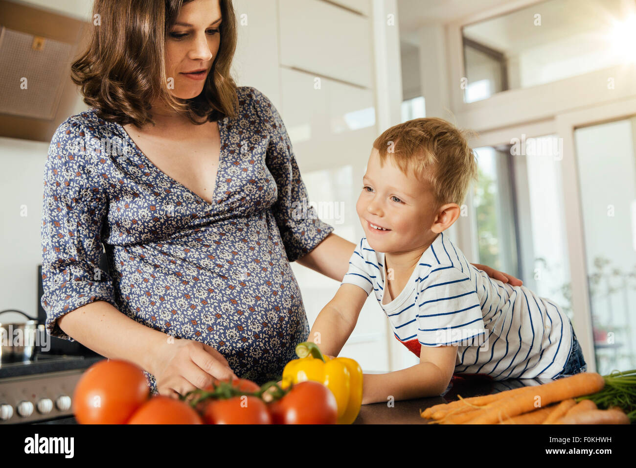 Pregnant woman with her little son in the kitchen preparing vegetables Stock Photo