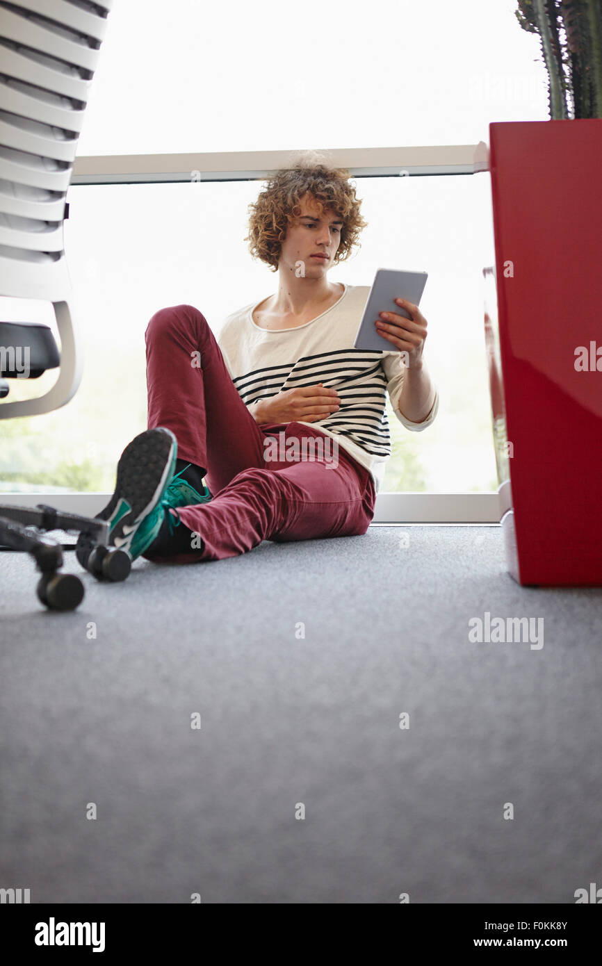 Young man in office sitting on floor using digital tablet Stock Photo