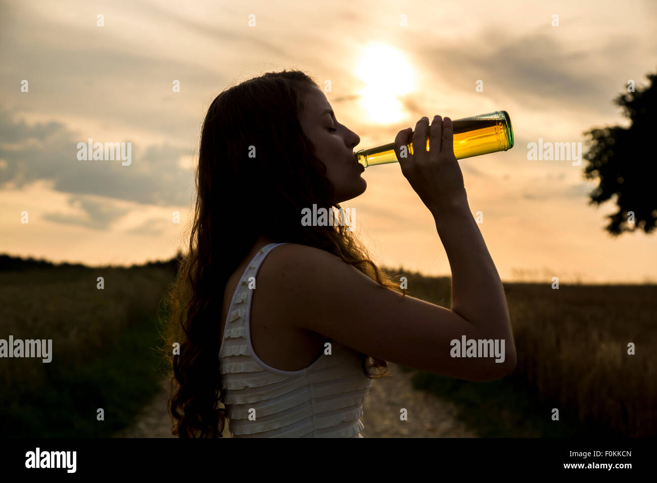 Young woman drinking from glass bottle, evening sonne Stock Photo Alamy