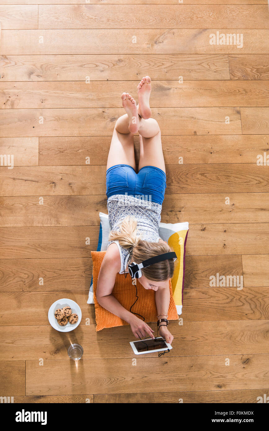Teenage girl lying on floor listening to music from digital tablet ...