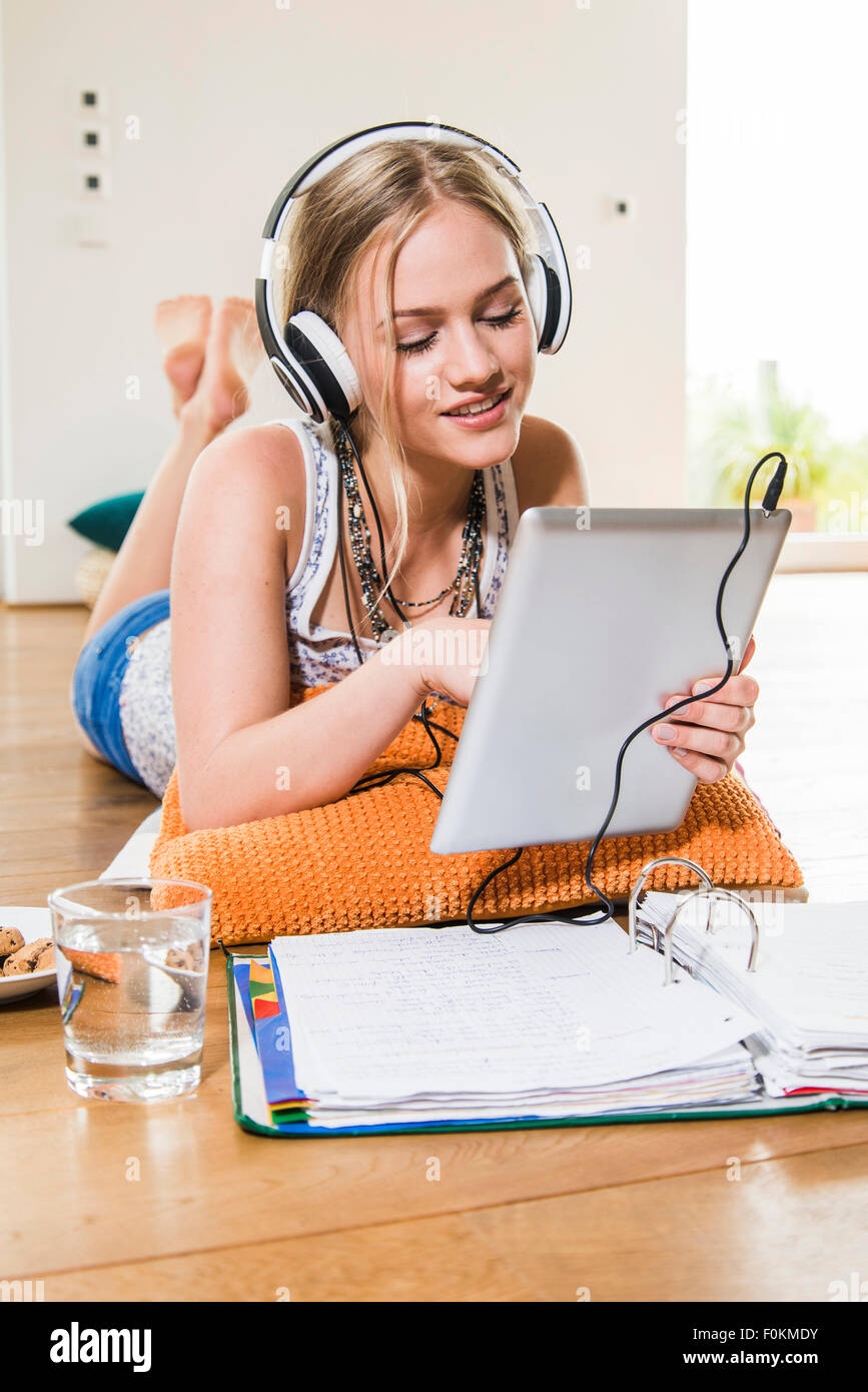 Teenage girl lying on floor listening to music from digital tablet ...
