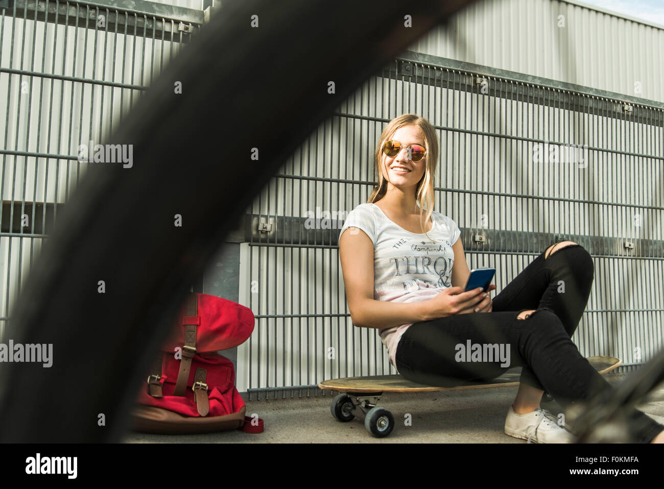 Teenage girl sitting on skateboard holding cell phone Stock Photo