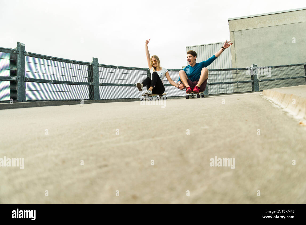 Enthusiastic young couple riding downhill with skateboards Stock Photo
