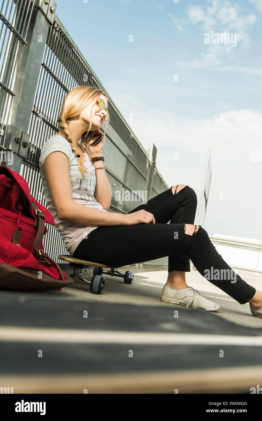Teenage girl sitting on skateboard talking on cell phone Stock Photo
